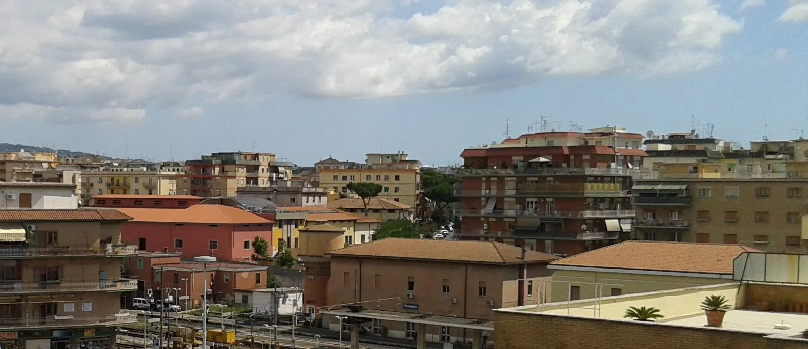 Tetti e palazzi di Ciampino visti dall'alto, con la stazione ferroviaria in primo piano e le colline sullo sfondo