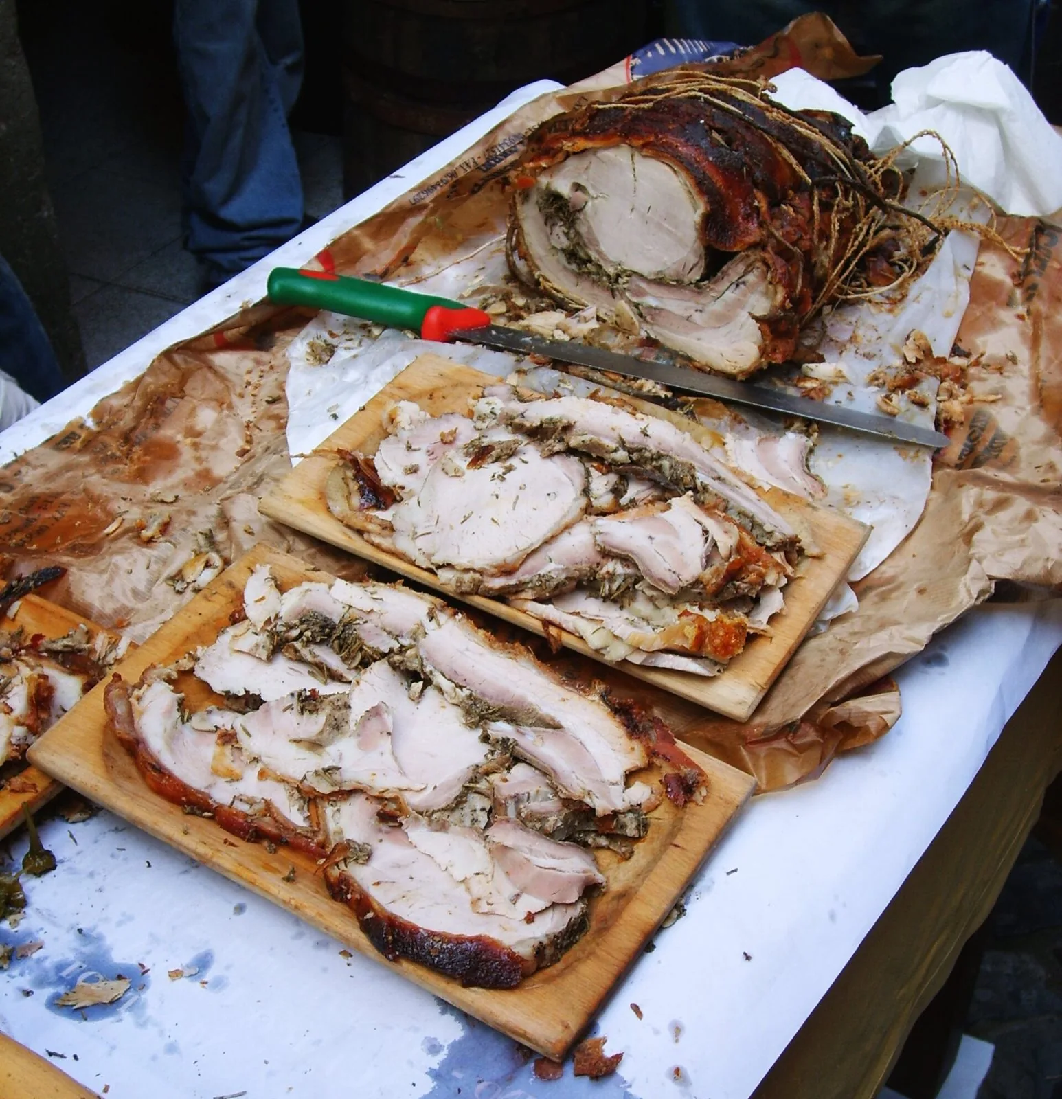 Porchetta affettata su taglieri di legno, con il rotolo intero dalla crosta dorata legato con lo spago